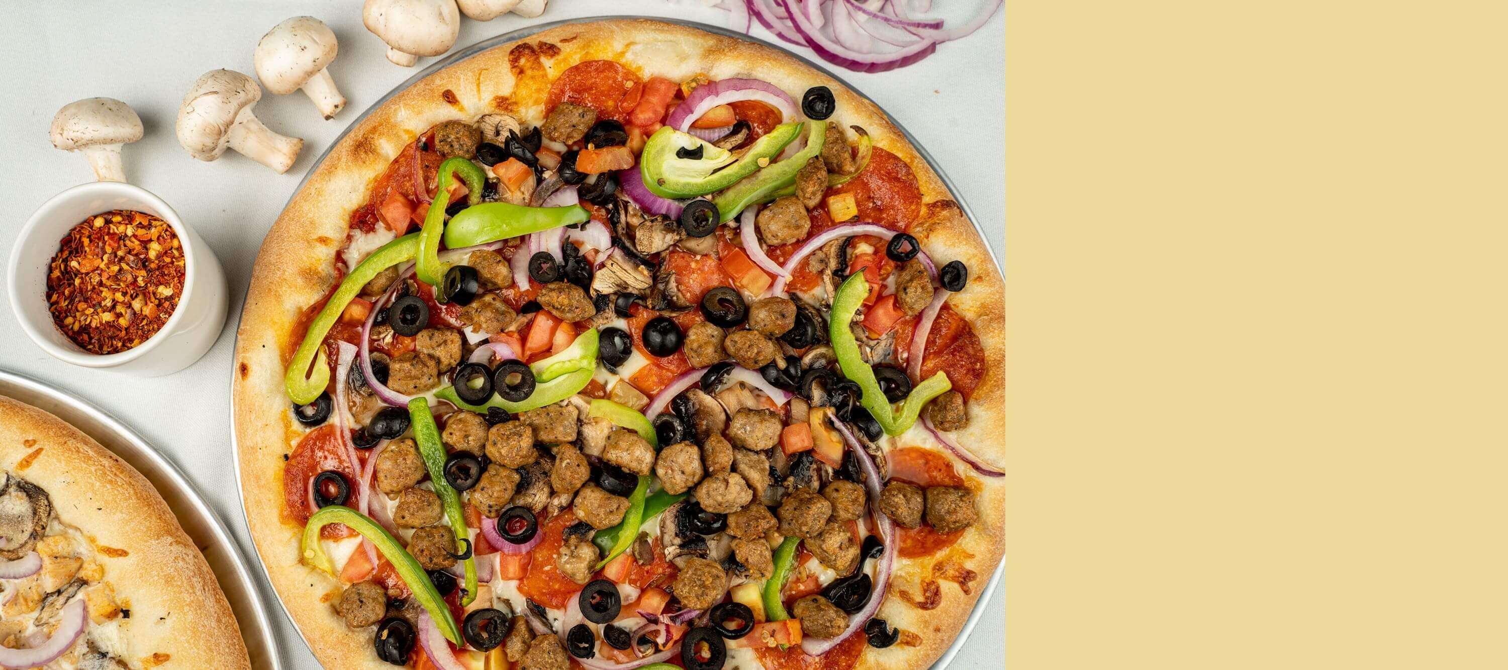 A pizza with meat, olives and peppers on it.